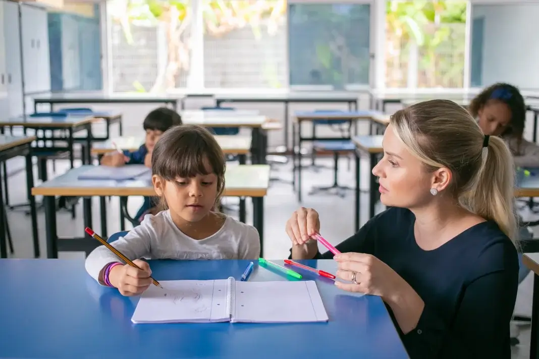 Dans une salle de classe, une professionnelle accompagne individuellement une élève dans une activité d’écriture, illustrant le soutien de proximité que les pôles d’appui à la scolarité (PAS) entendent renforcer auprès des élèves à besoins éducatifs particuliers.