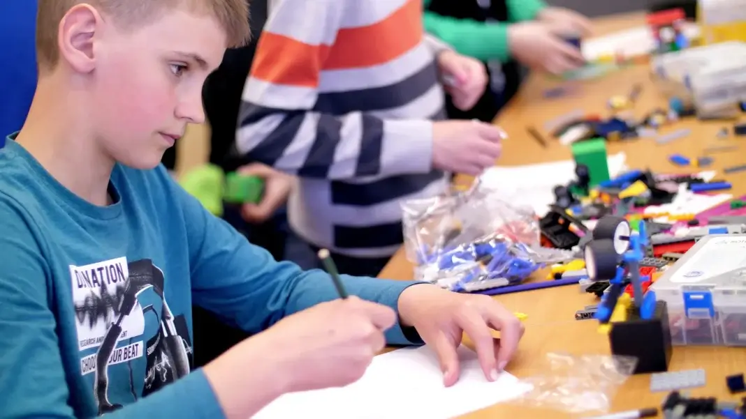 Un enfant dessine un projet de construction lors d’un atelier collectif, illustrant l’importance de proposer des accompagnements diversifiés et adaptés aux besoins de chaque enfant dans le cadre de la transformation de l’offre en protection de l’enfance.